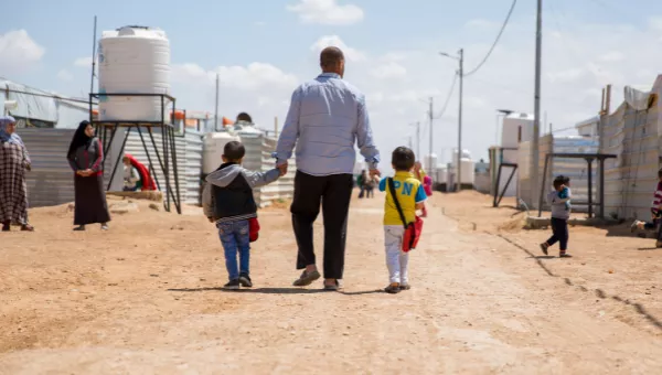 A father walks down the road holding his childrens hands in the displacement camp they live in, in Iraq.