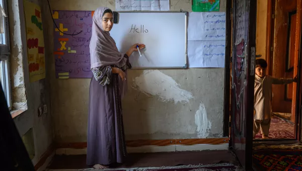 Young teen girl stands in front of whiteboard with "Hello" written.