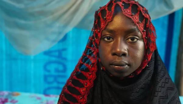 Young girl wearing black and red hijab looking straight into camera.