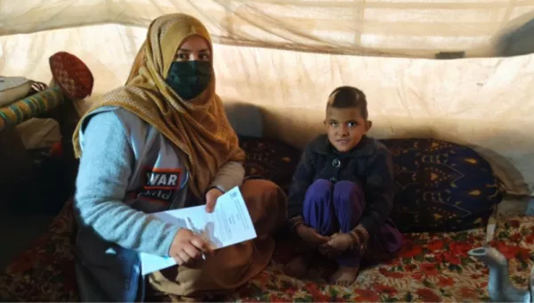 War Child Staff Member sat on a carpet with a young Afghan girl