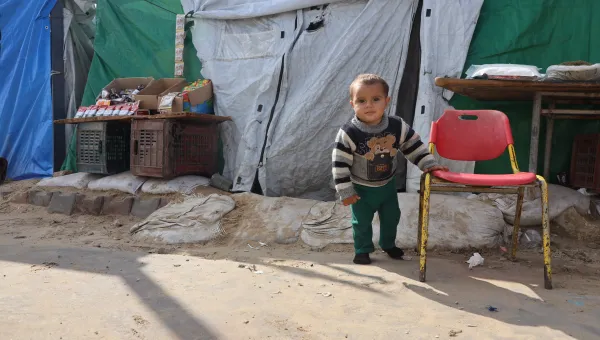 small toddler stands in front of tent at IDP camp in Gaza