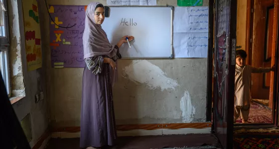 Young teen girl stands in front of whiteboard with "Hello" written.