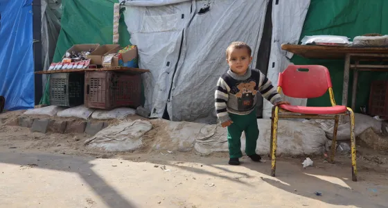 small toddler stands in front of tent at IDP camp in Gaza