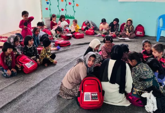Kids sitting in groups with War Child branded back packs 