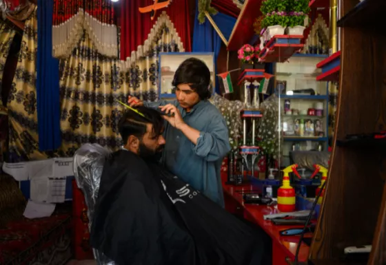 Afghan young person cutting an adult's hair.
