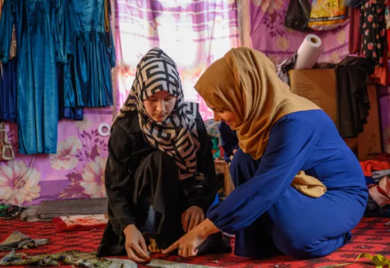 Afghan woman mentor helping her mentee with sewing.
