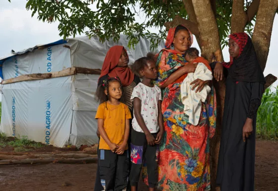 Young Sudanese girl, standing with her host family, with their tent in the background.