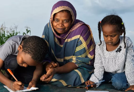 Mother smiling, whilst her children beside her do their educational work.