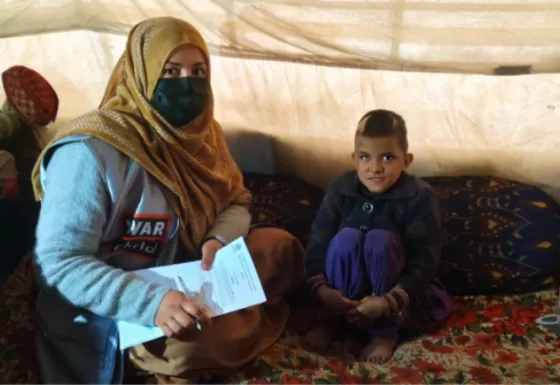 War Child Staff Member sat on a carpet with a young Afghan girl