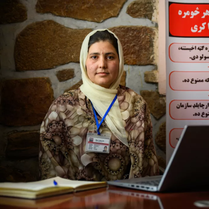 Afghan women standing behind a desk with a laptop open.