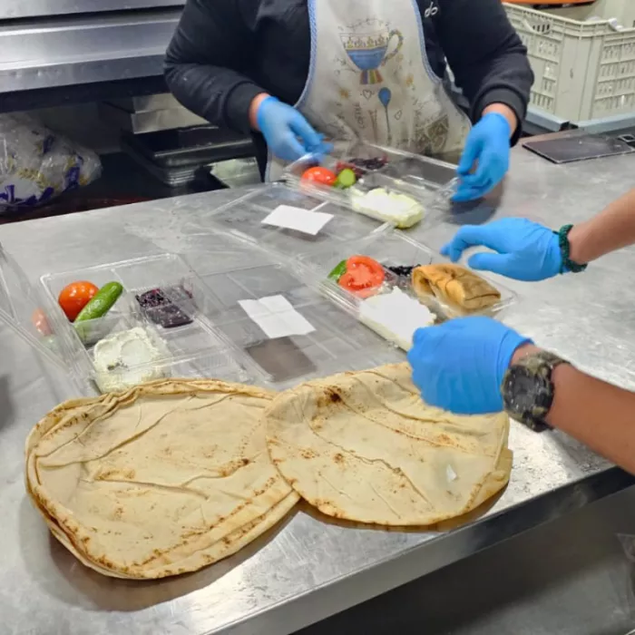 Kitchen showing hands assembling food boxes.