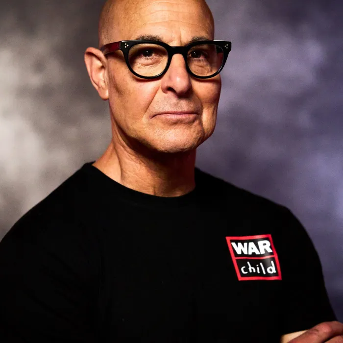 Stanley Tucci looking at camera wearing War Child t shirt